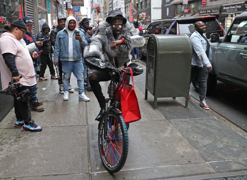 Brown riding a bicycle down a Manhattan sidewalk.