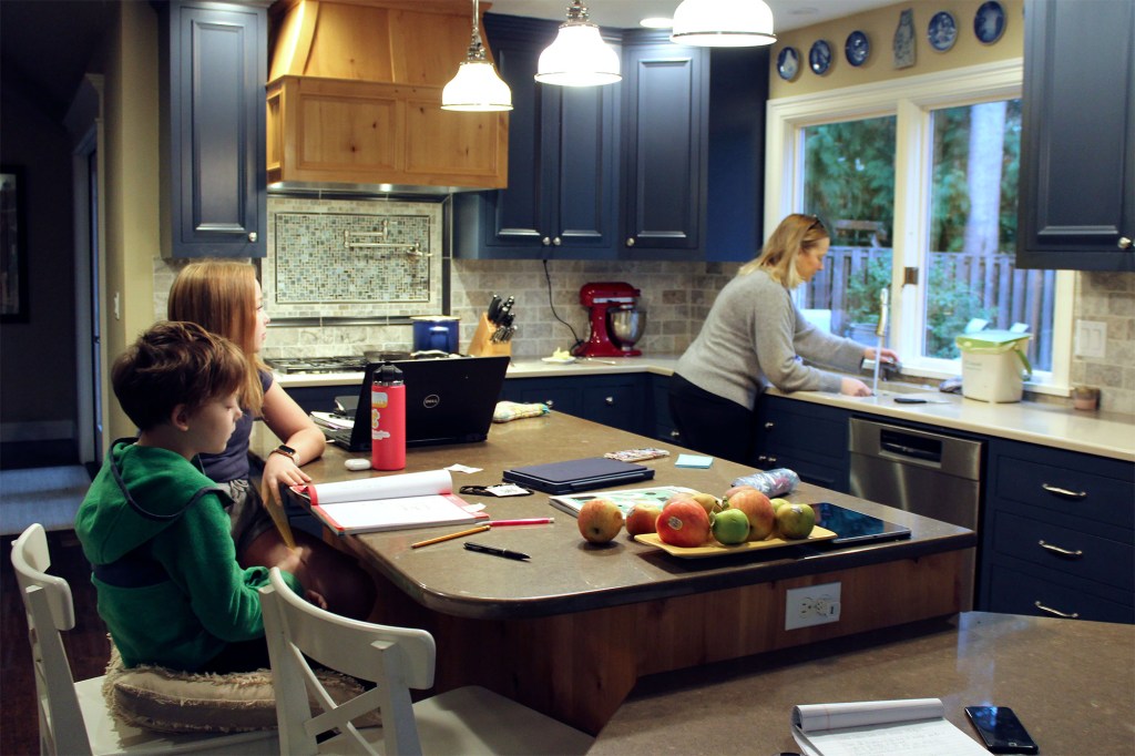 Charlie Dale, left, works on his math notebook with help from his older sister Maddi Dale as their mother cooks pancakes in their home in Lake Oswego, Ore., Oct. 30, 2020.