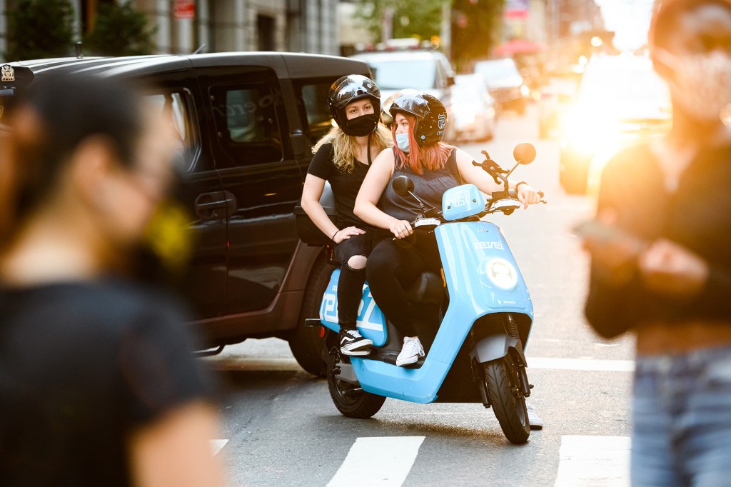 People ride a Revel scooter through traffic.