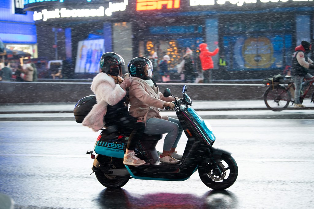 People ride a Revel scooter.