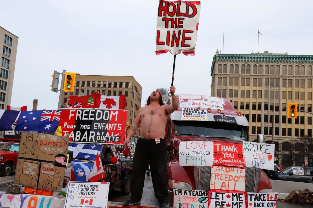 A person holds a sign in front of trucks blocking a downtown street as truckers and their supporters continue to protest against coronavirus disease (COVID-19) vaccine mandates in Ottawa, Ontario, Canada.