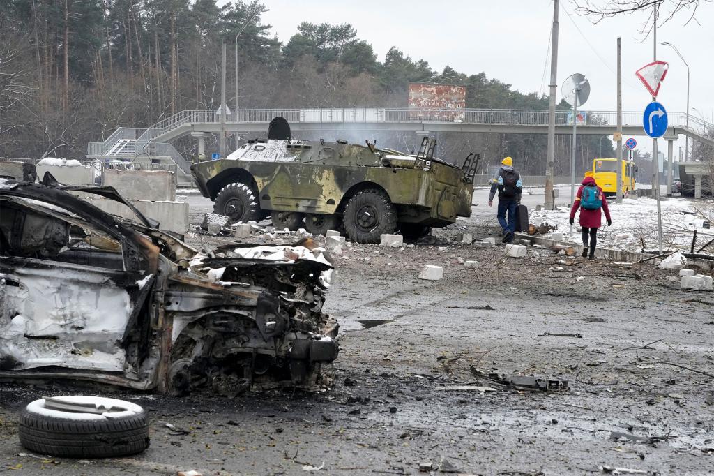 People walk by a damaged vehicle and an armored car at a checkpoint in Brovary, outside Kyiv, Ukraine, Tuesday, March 1, 2022.