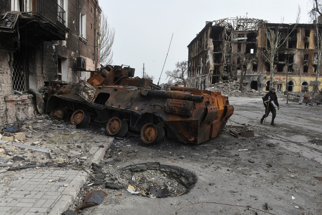 A man walks past a burnt armoured personnel carrier near buildings destroyed in the course of Ukraine-Russia conflict in the southern port city of Mariupol, Ukraine April 1, 2022. 