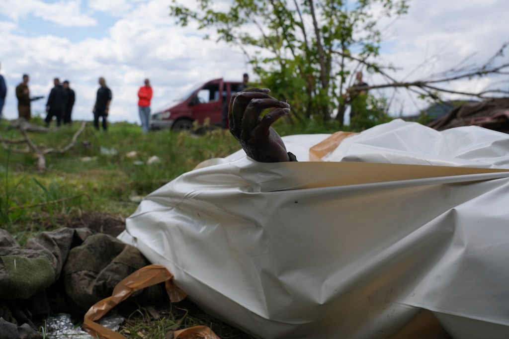 The hand of a dead Russian soldier pokes out of a body bag during the exhumation of killed Russian soldiers near the village of Malaya Rohan on May 18, 2022. 