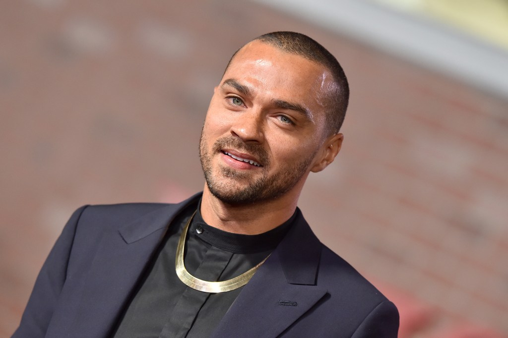 Jesse Williams in a dark suit with a gold necklace.