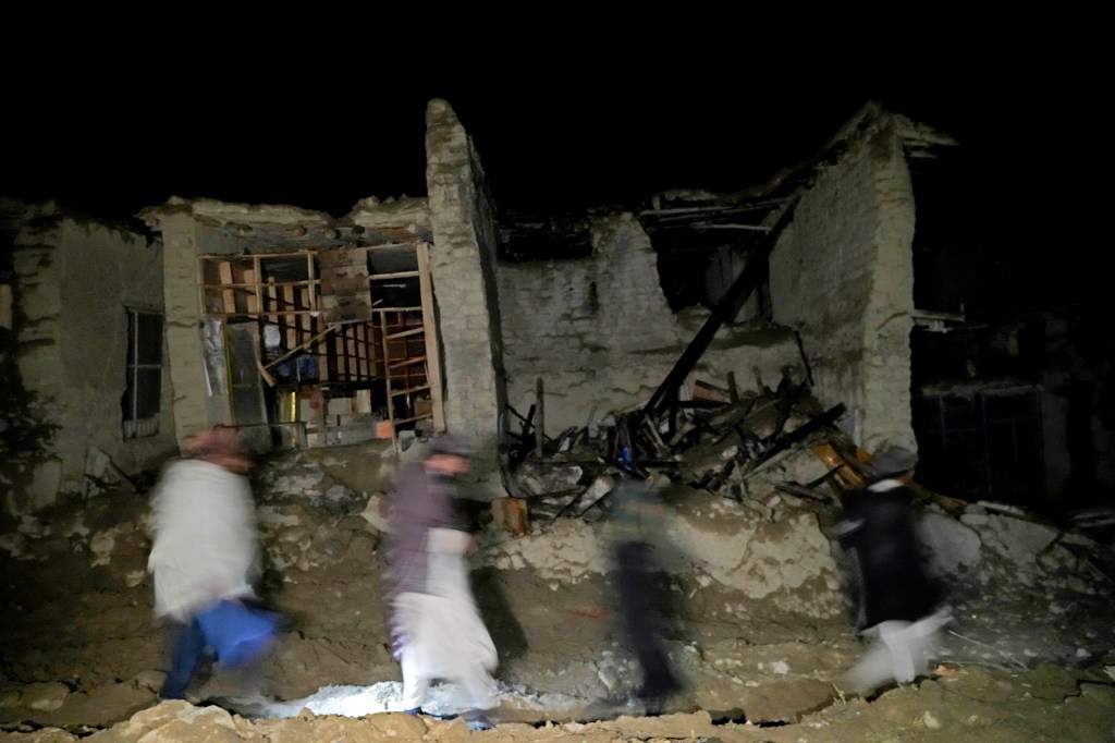 Afghans walk by a destroyed housein the village of Gyan, in Paktika province, Afghanistan.