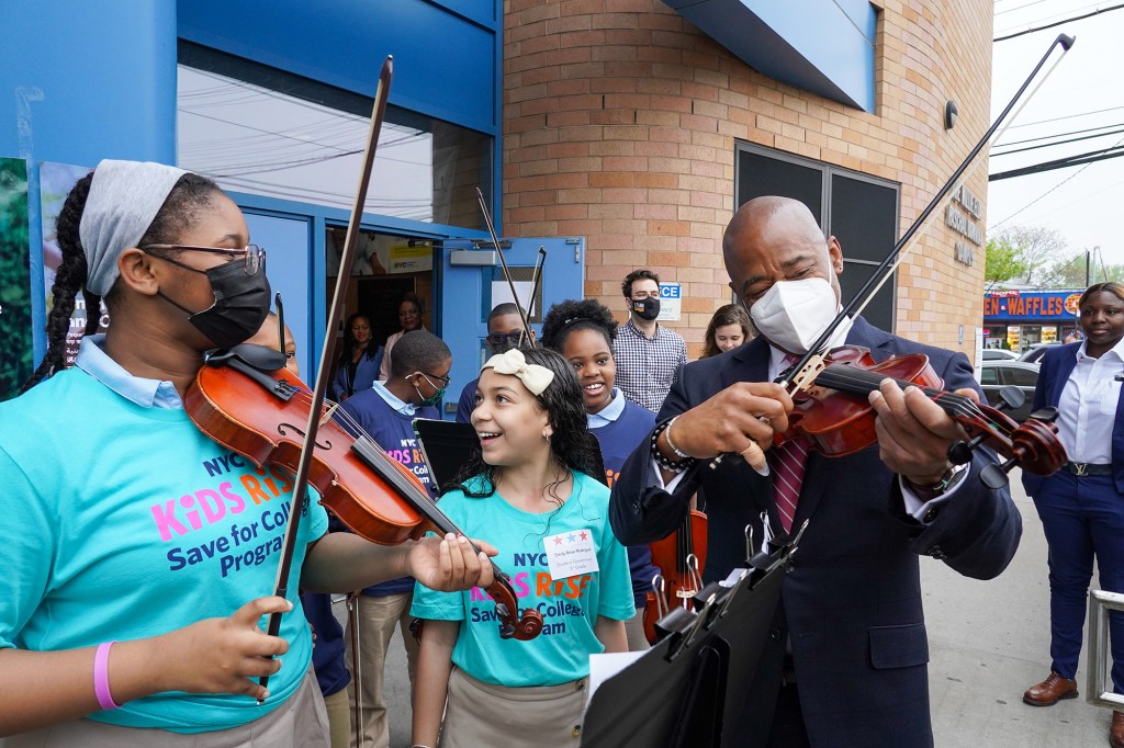 Mayor Eric Adams picks up a violin with student orchestra at entrance of PS 169.