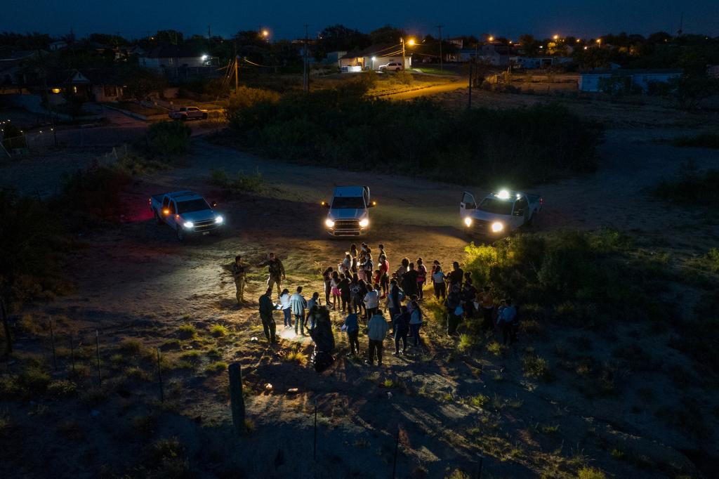 Texas Army National Guard and border patrol vehicle lights point towards asylum seeking migrants from Central and South America, who earlier crossed the Rio Grande river into the U.S. from Mexico, as they are prepared for registration, in Roma, Texas, U.S., June 9, 2022.