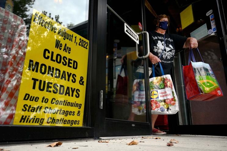 A woman exits a shop displaying a sign announcing reduced store hours due to the a staff shortage.