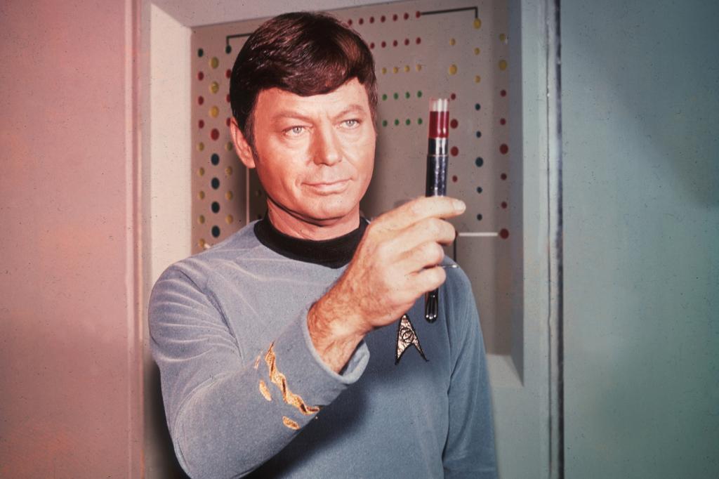 American actor DeForest Kelley (1920 - 1999), portraying Dr 'Bones' McCoy, examines a vial filled with a dark substance in a still from the television show, 'Star Trek,' 1960s.