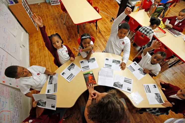 Teacher Rachel Mann sits at a horse-shoe shaped desk with seven of her second grade students.