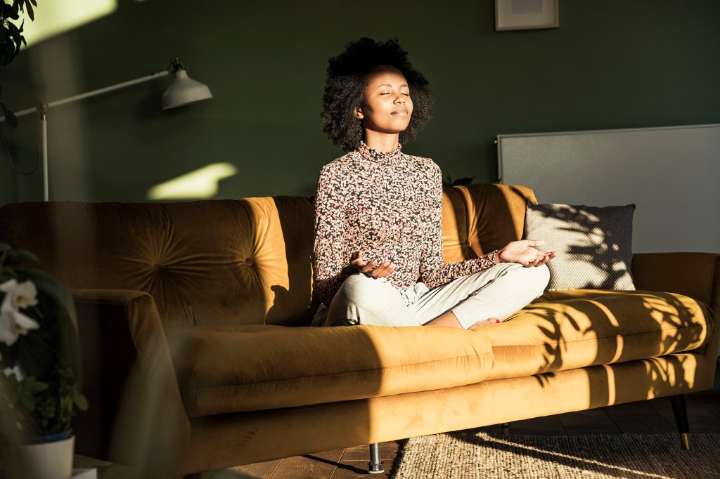 Woman meditating while sitting on sofa at home.