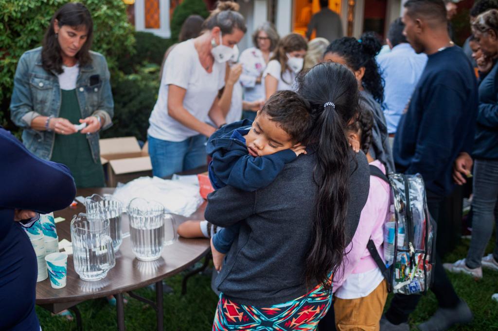 A woman, who is part of a group of immigrants that had just arrived, holds a child as they are fed outside St. Andrews Episcopal Church.