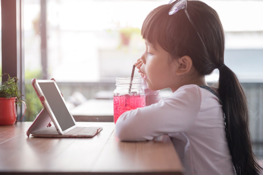 A kid watches her iPad and eats.