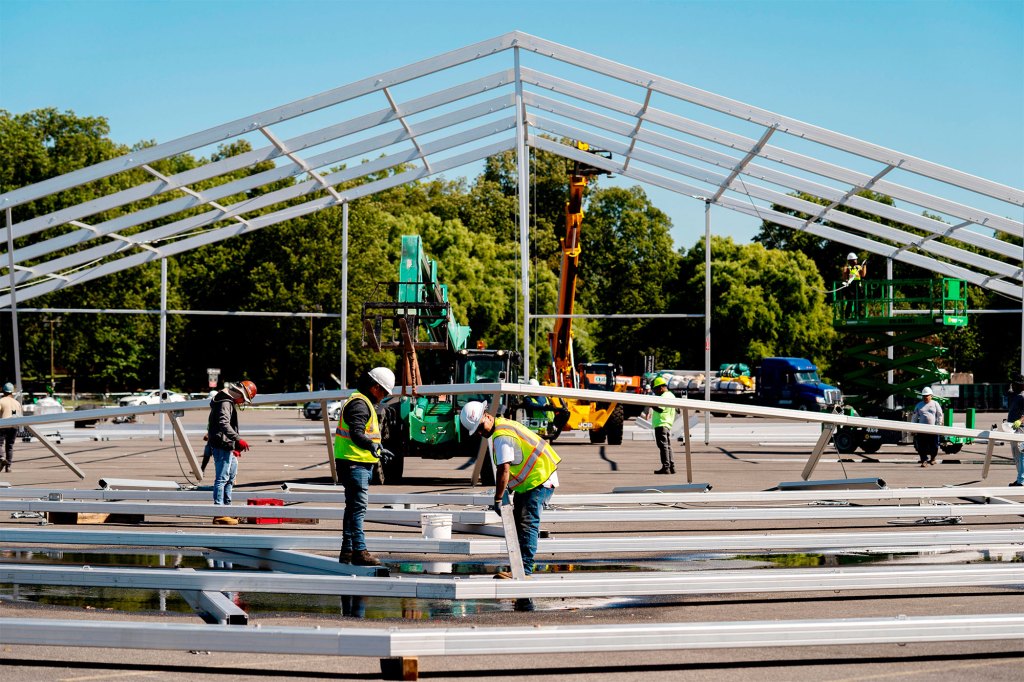 A picture of workers working on a hangar-sized tent in the parking lot of Orchard Beach in the Bronx.