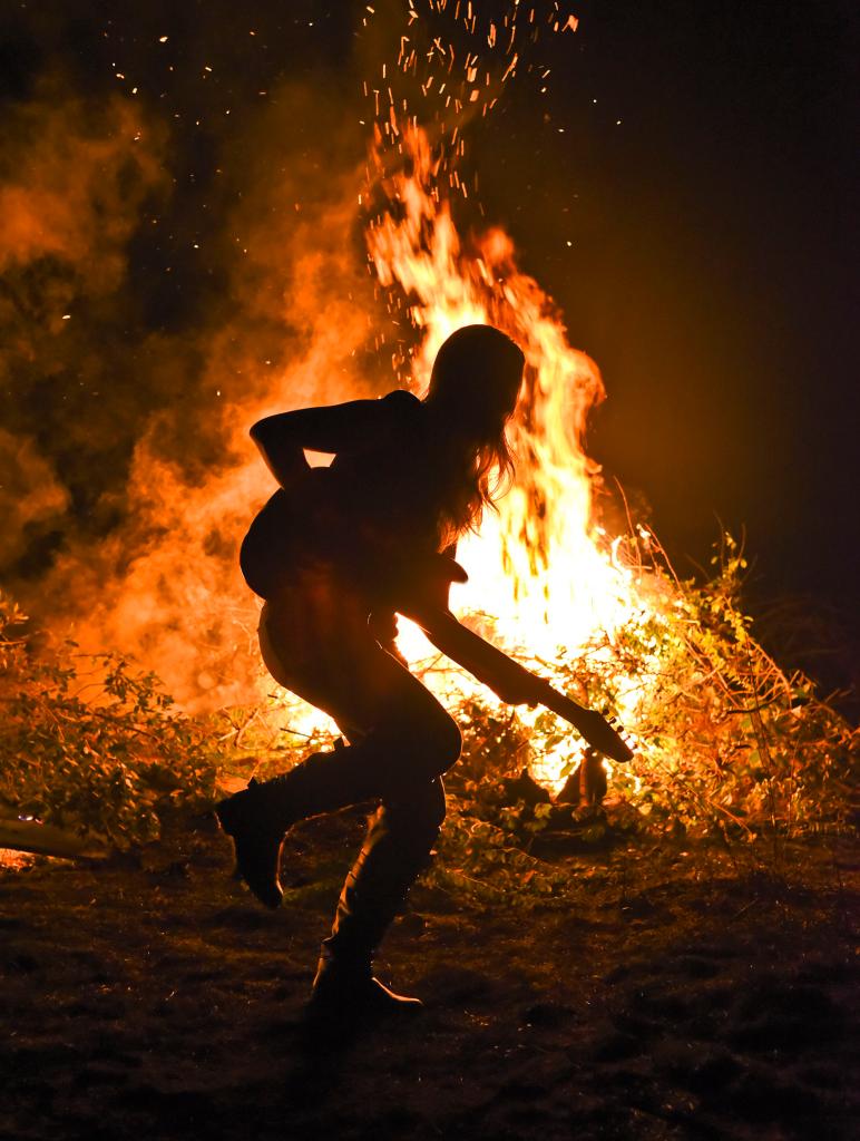 Woman playing electric guitar at a bonfire party. Northern California.