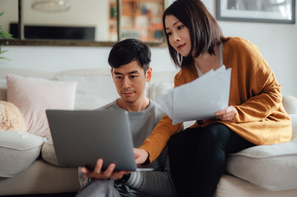 man and woman comparing notes on paper with computer screen