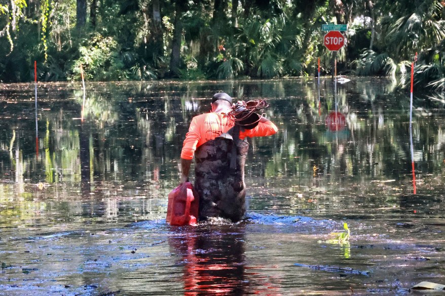 Carrying a gas can and a sump pump, resident Cody Clark walks into waist-high water to his flooded home on Crossover Lane along the shore of Lake Harney in Geneva, Florida.