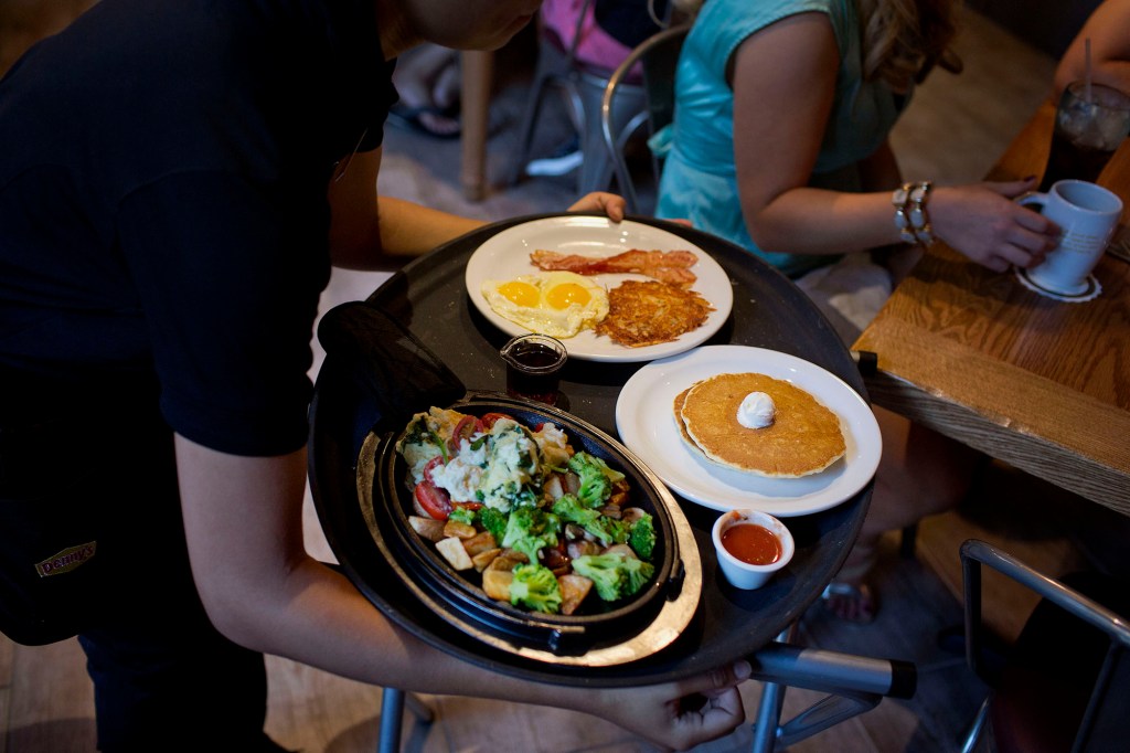 A Denny's waiter serving diners with a tray of food.