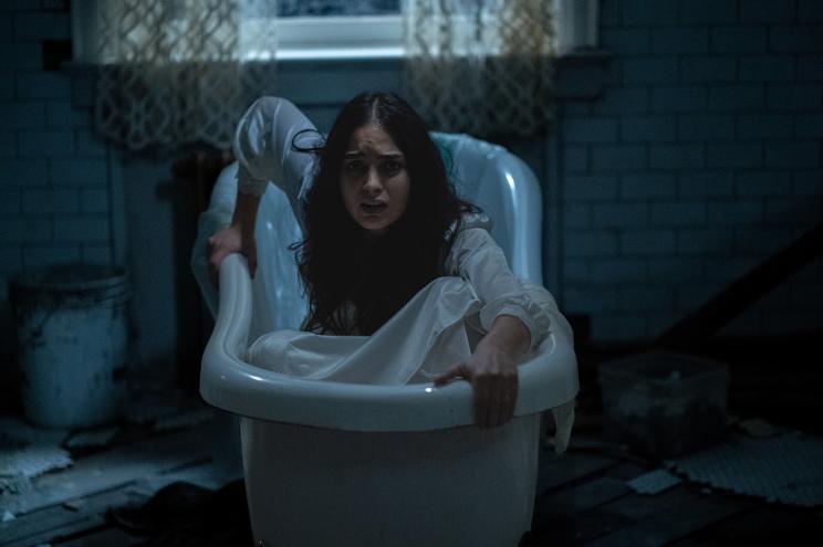 Melissa Barrera in a scene from "Bed Rest." She's crouching in a bathtub, wearing a nightgown, and is look ahead, horrified.