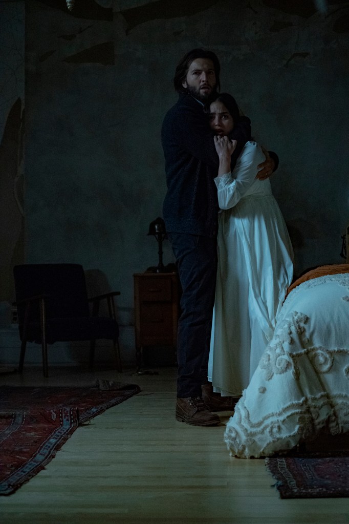 Melissa Barrera and Guy Burnet as Julie and Daniel looking suitably horrified in "Bed Rest." They're clutching each other in a bedroom and looking straight ahead. Julie is wearing a nightgown.