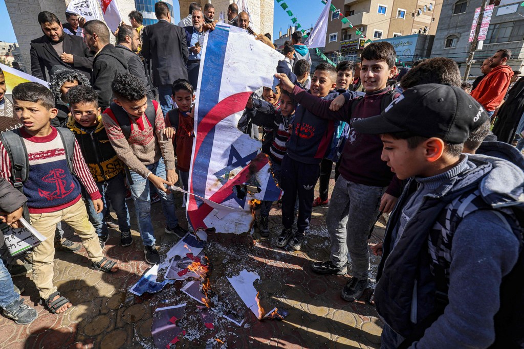 Palestinian protesters burn the Israeli flag and deface posters depicting  Netanyahu.