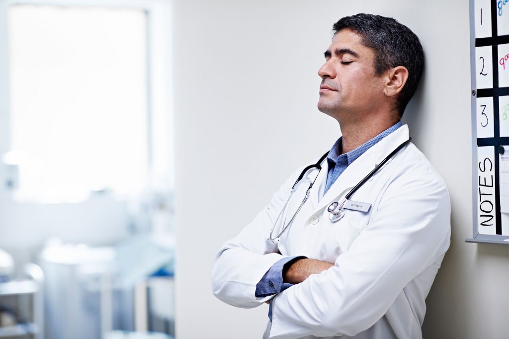 Shot of a tired doctor leaning against the wall in a hospital