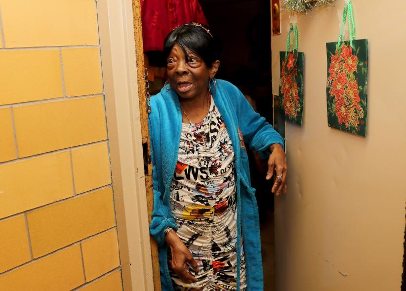 an older woman in her bathrobe stands at her door