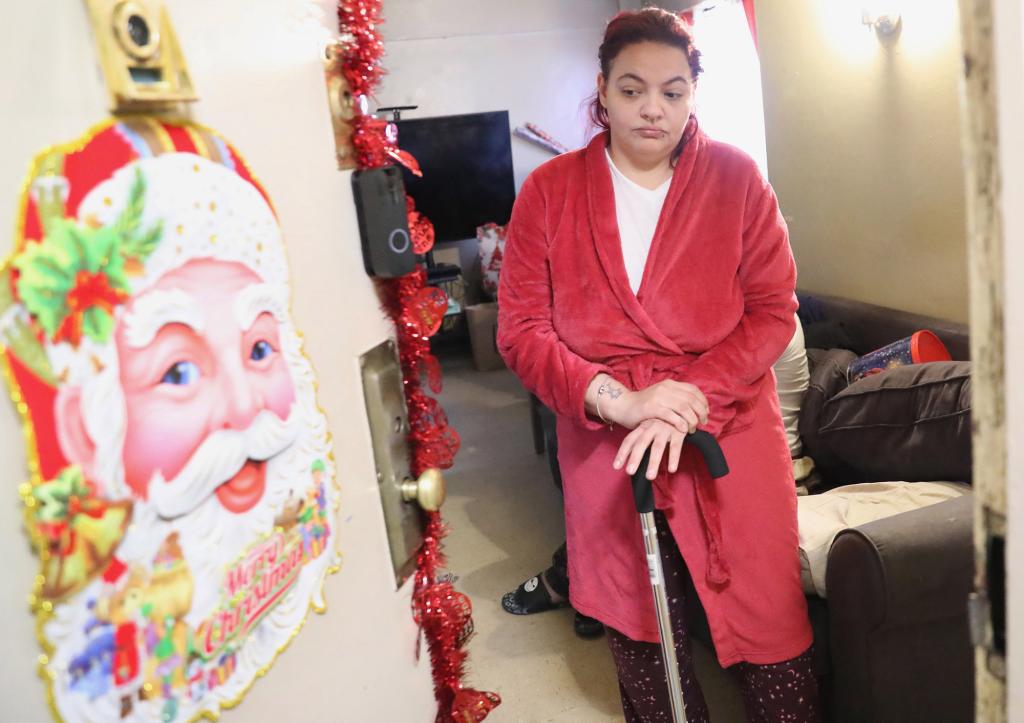 A woman in a red bathrobe stands at the door of her apartment, which is decorated for Christmas