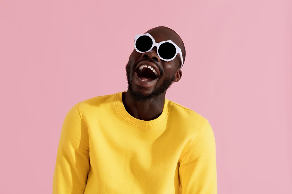 Man against pink background wearing yellow sweater and glasses