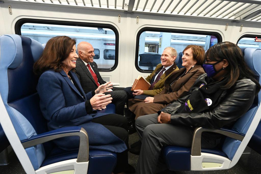 Gov. Kathy Hochul (closest left) sits next to SMART chief Anthony Simon (furthest left) as she travels aboard a LIRR train to the ribbon cutting for Third Track. The pair sit opposite from MTA chairman Janno Lieber (far right) and interim LIRR president Catherine Rinaldi (middle right) and a home health aide, Robin Allen (closest right).