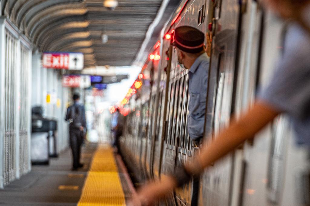 Two conductors are pictured aboard a Long Island Rail Road train -- one leaning out a window while another looks out a door -- at the commuter connector's major Jamaica hub in Queens in 2020. A Post investigation revealed the LIRR has overstaffed the position, costing riders millions.