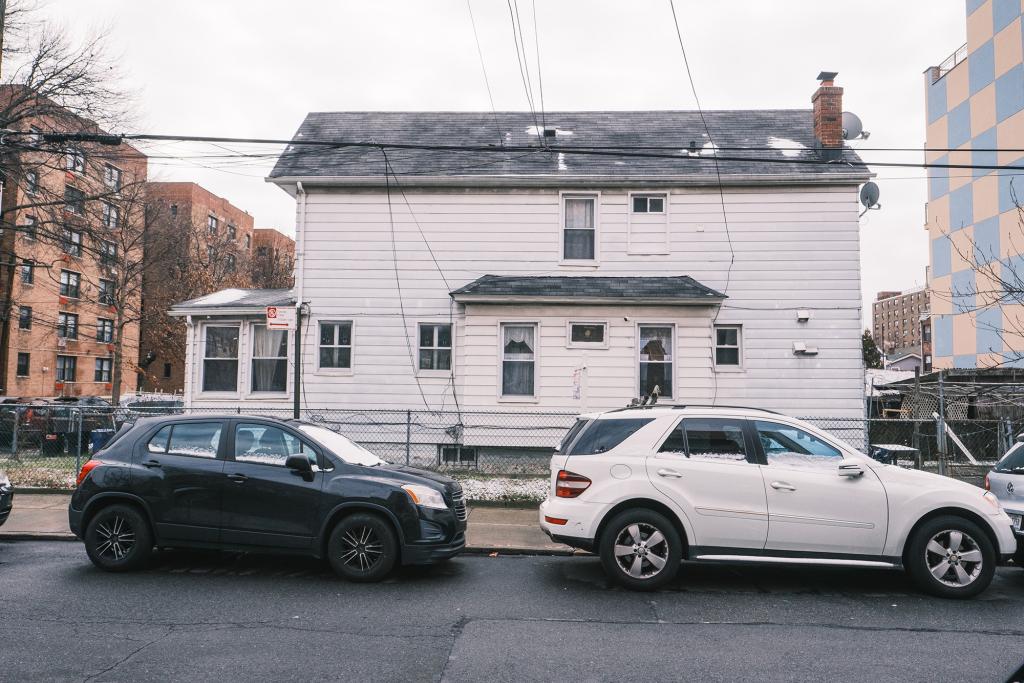 A side view of a Queens single family home with two cars in front of it.