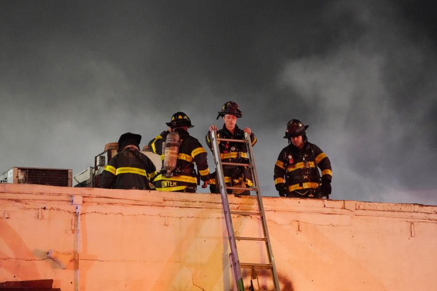 Firefighters at the top of the building with a ladder.