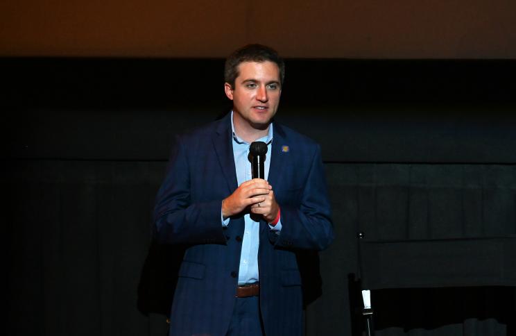 James Skoufis in a dark photo holding a microphone while standing with a jacket on