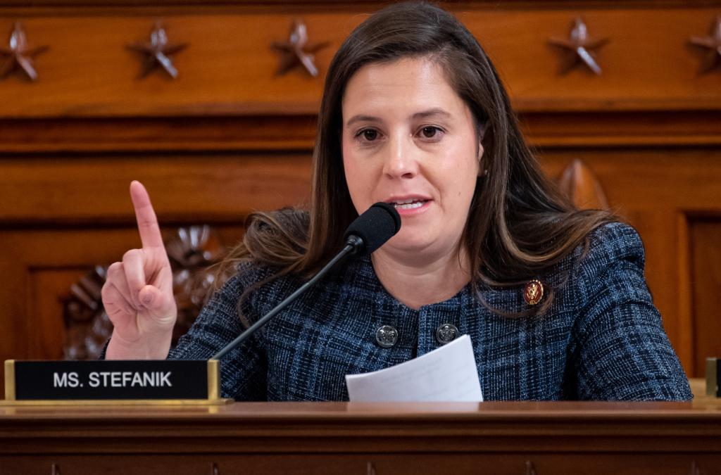 Stefanik sitting at a congressional hearing with an index finger pointing up