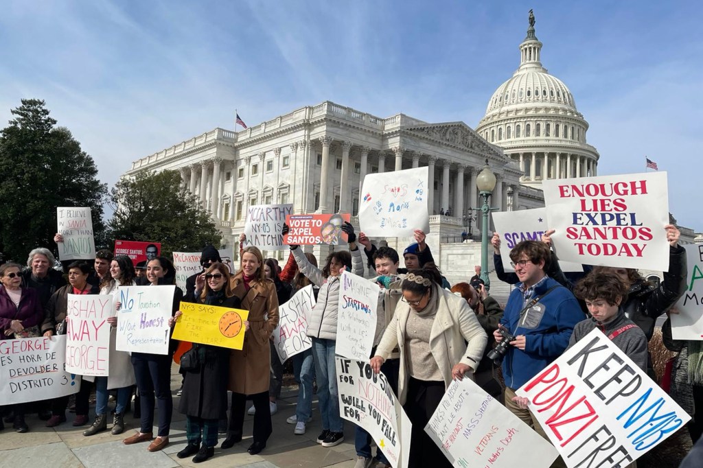 A crowd of people holding protest signs with the US Capitol in the background.