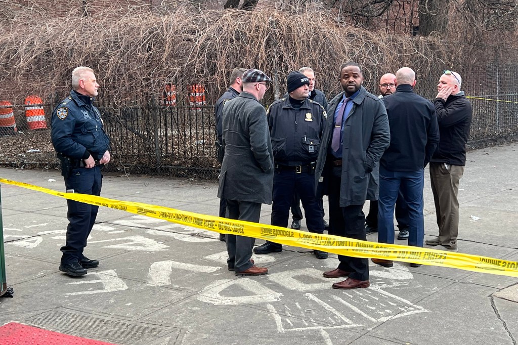 Several police officers crowded around a sidewalk area marked off by crime scene tape.