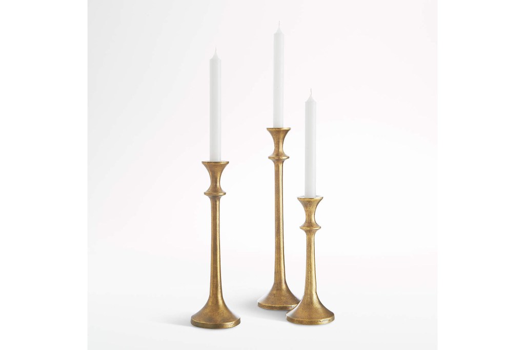 three gold brass candle holders with white candles on top