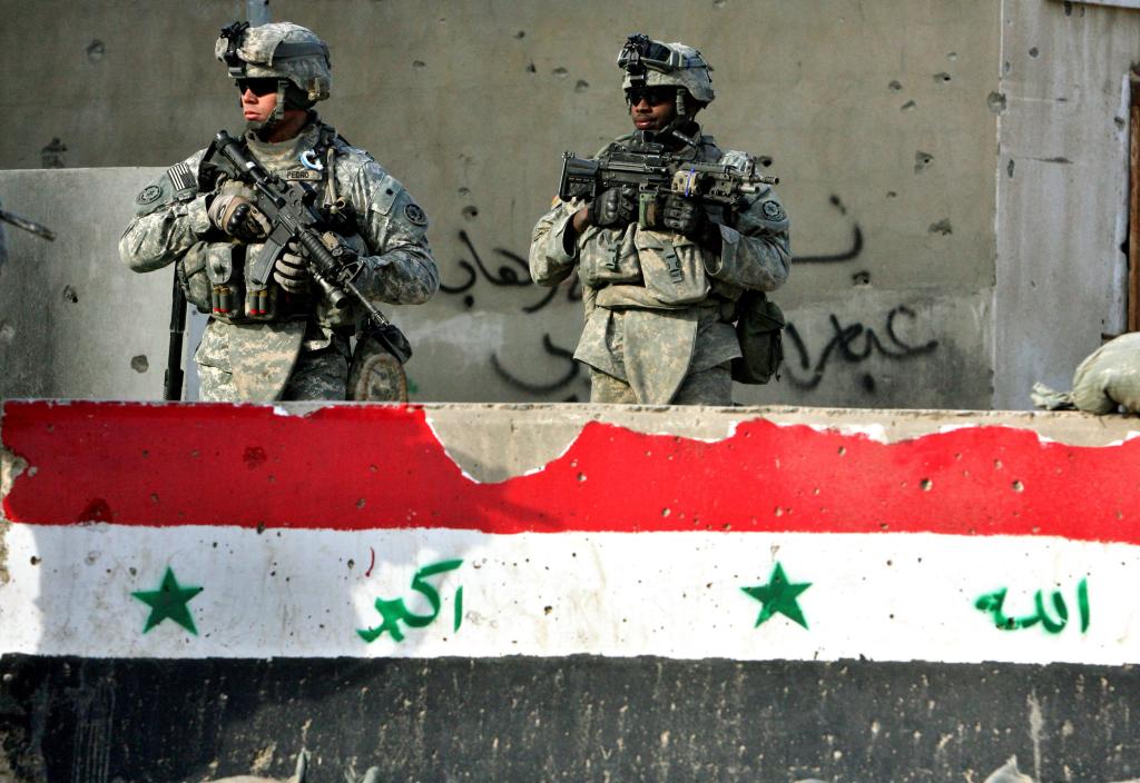 Two US soldiers from the 2nd Squadron, 2nd Stryker Cavalry Regiment walk past a concrete block with a painted-on Iraqi flag.