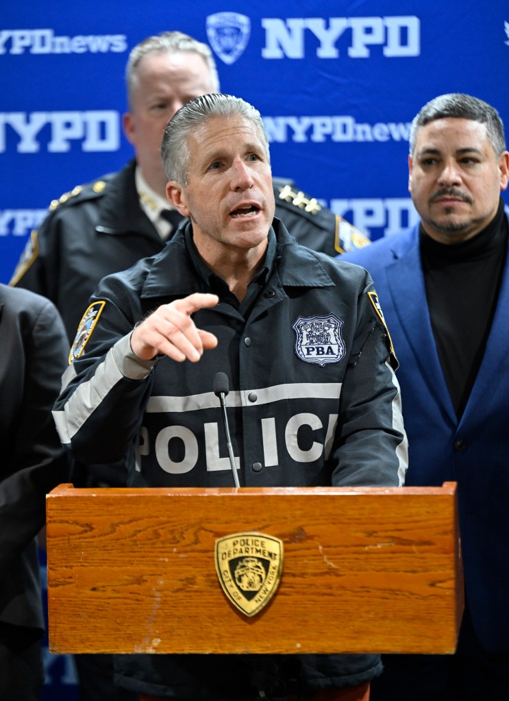 Pat Lynch pointing at something while speaking at a podium with other men behind him