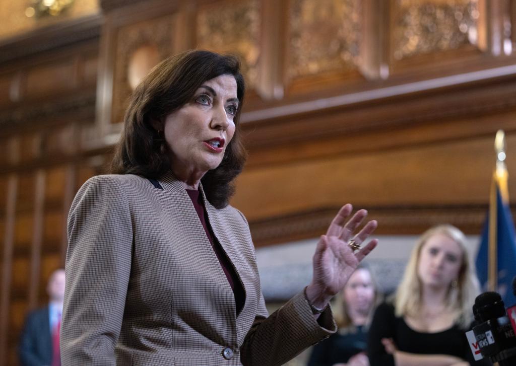 Kathy Hochul speaking in an ornate room with people in background.