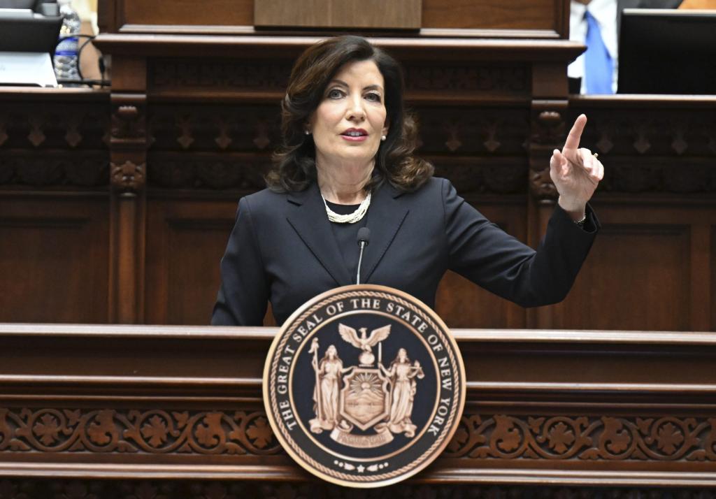 Kathy Hochul speaking at a wooden rostrum with a raised hand