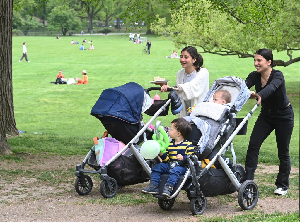 Two young women pushing strollers in central park. 