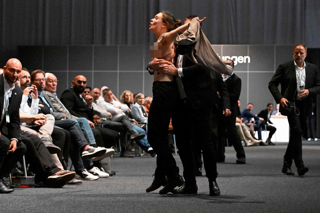 A topless activist is escorted away at Volkswagen’s annual meeting.