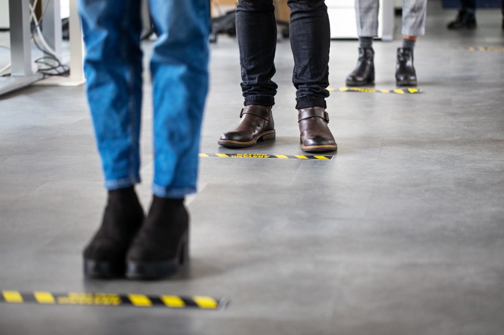 Low angle shot of business people standing behind social distancing signage on office floor. 