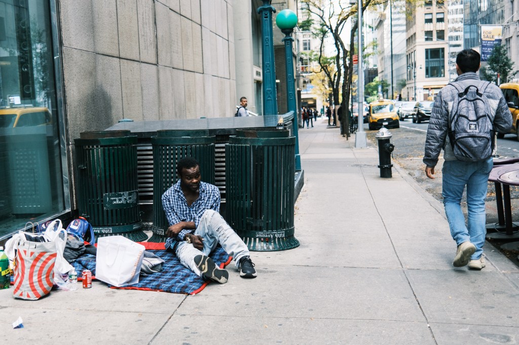 A homeless man with his belongings and a makeshift shelter of trashcans on the sidewalk in midtown Manhattan.