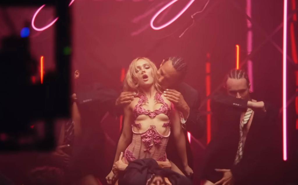 Lily Rose Depp in a tight outfit making a weird face with a man draped over her. 