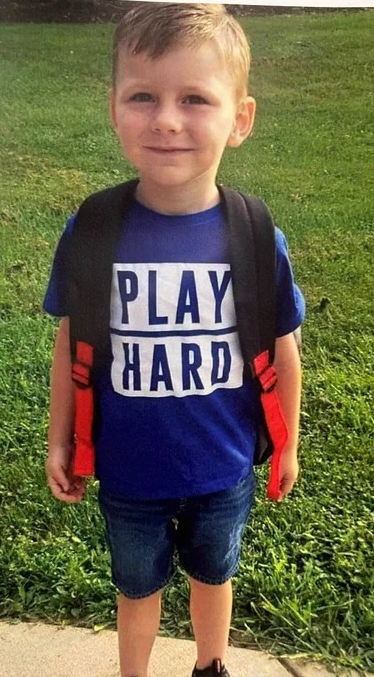 Landon Maloberti smiles as he stands in front of a grassy lawn with a backpack on. 