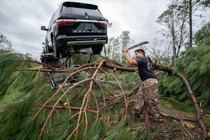 A man used a machete to clear fallen trees and branches around a vehicle near Madison, Florida.